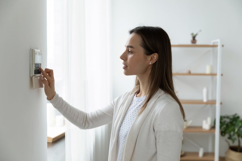 Young woman using thermostat on wall